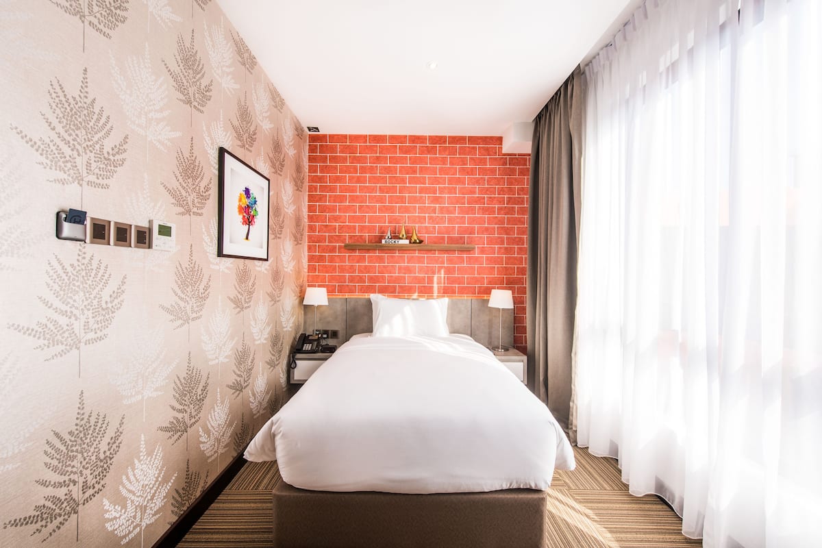 A hotel room with a bed, a nightstand, a phone, a framed picture, and a shelf with decorative items.