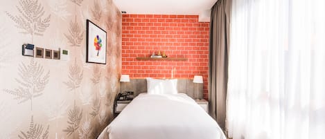A hotel room with a bed, a nightstand, a phone, a framed picture, and a red brick accent wall.