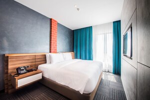 Une chambre d’hôtel moderne avec un grand lit, une tête de lit en bois, une table de chevet avec un téléphone et un téléviseur fixé au mur.