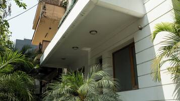 A modern building with a balcony, surrounded by lush greenery and potted plants.