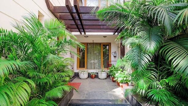 Una entrada techada con una pérgola de madera, plantas en macetas y un sendero empedrado que lleva a una puerta.