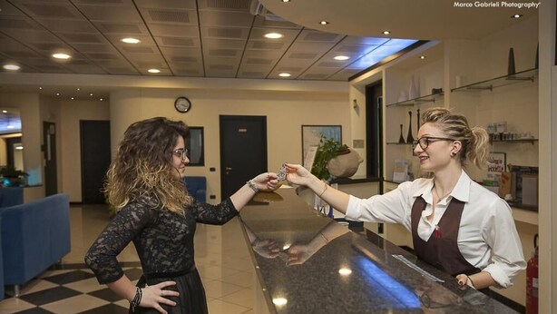 A reception area with a check-in counter, a clock on the wall, and a potted plant. - Hotel Bussana (Porto Tolle)