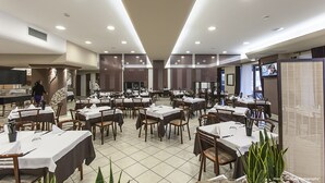 A spacious restaurant with multiple tables and chairs, a tiled floor, and recessed ceiling lights. - Hotel Bussana (Porto Tolle)