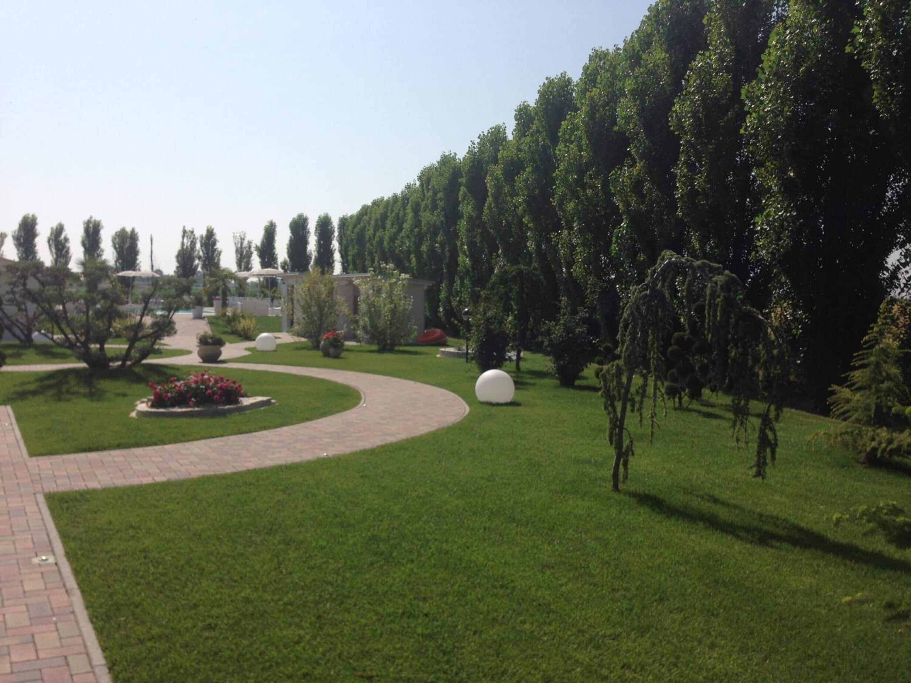 Un jardin aménagé avec un sentier sinueux, divers arbustes et une grande sculpture sphérique.