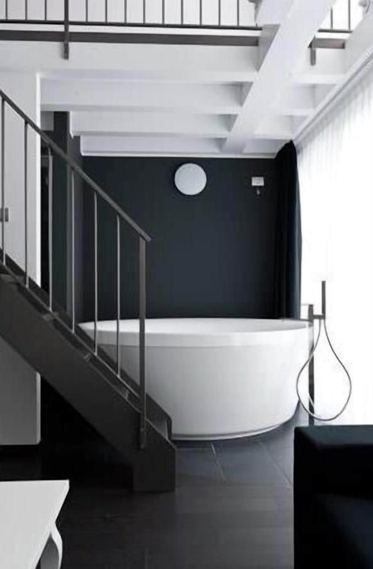 Une salle de bain moderne avec une baignoire sur pieds, un escalier et un design minimaliste.