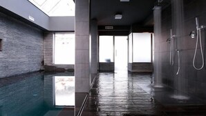 A modern indoor pool area with a glass ceiling, a wet floor, and a shower area with multiple faucets. - Muu Village (Folgaria)