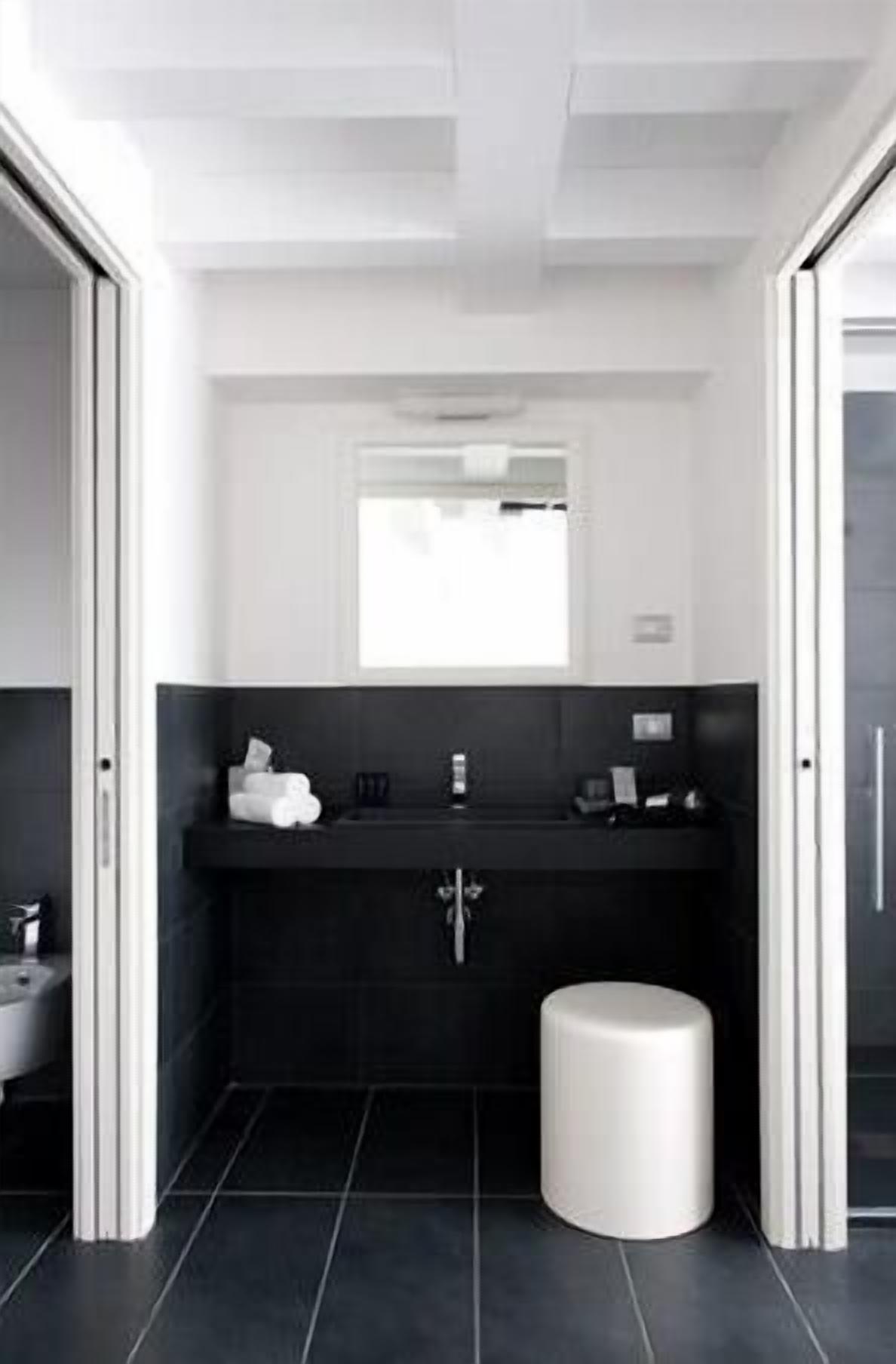Un baño moderno con un tocador negro, un lavamanos blanco y un taburete blanco pequeño.
