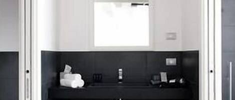 Un baño moderno con un tocador negro, un lavamanos blanco y un taburete blanco pequeño.