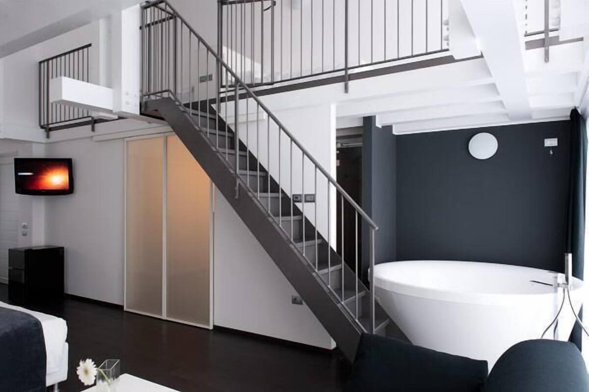 A modern living room with a staircase, a flat-screen TV, a large white bathtub, and a dark wall with a circular feature.