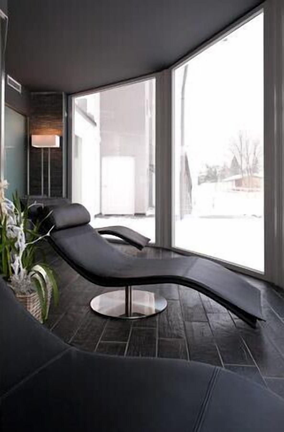A modern lounge area with a curved black lounge chair, a small side table, and a potted plant.
