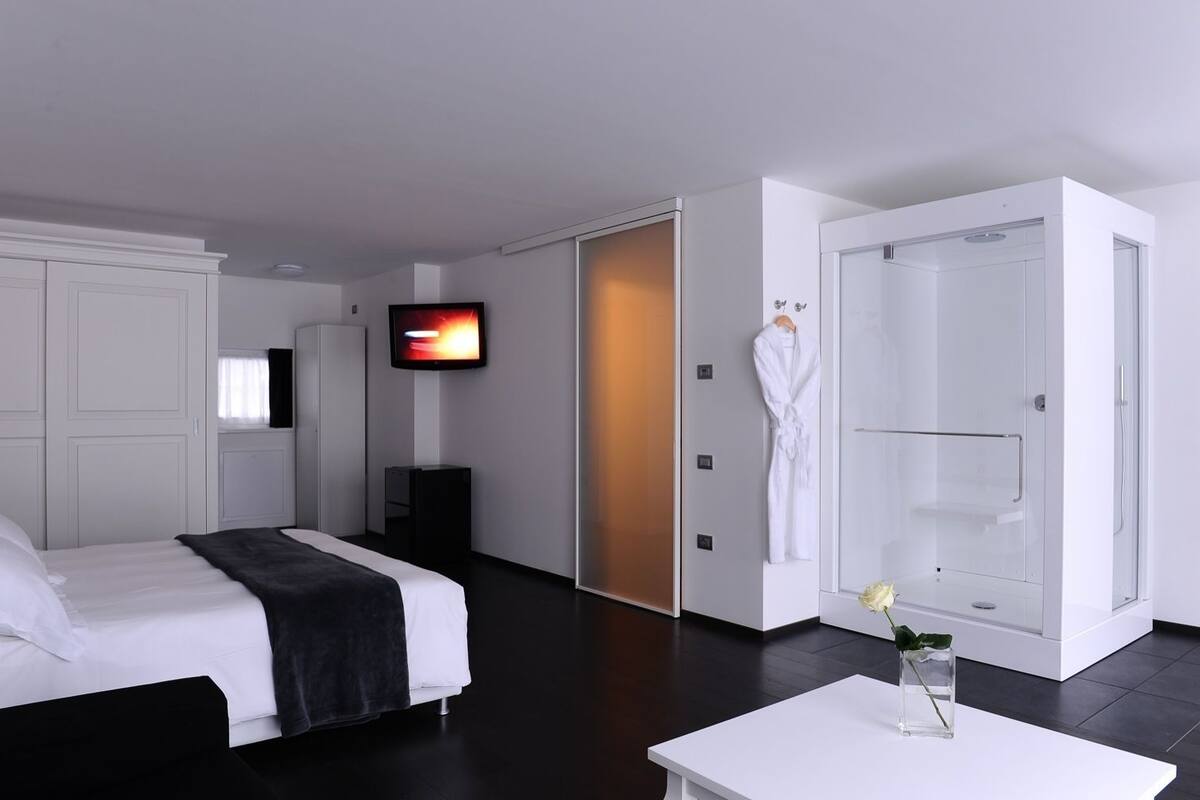 A modern hotel room with a bed, a TV, a robe hanging, and a shower area.