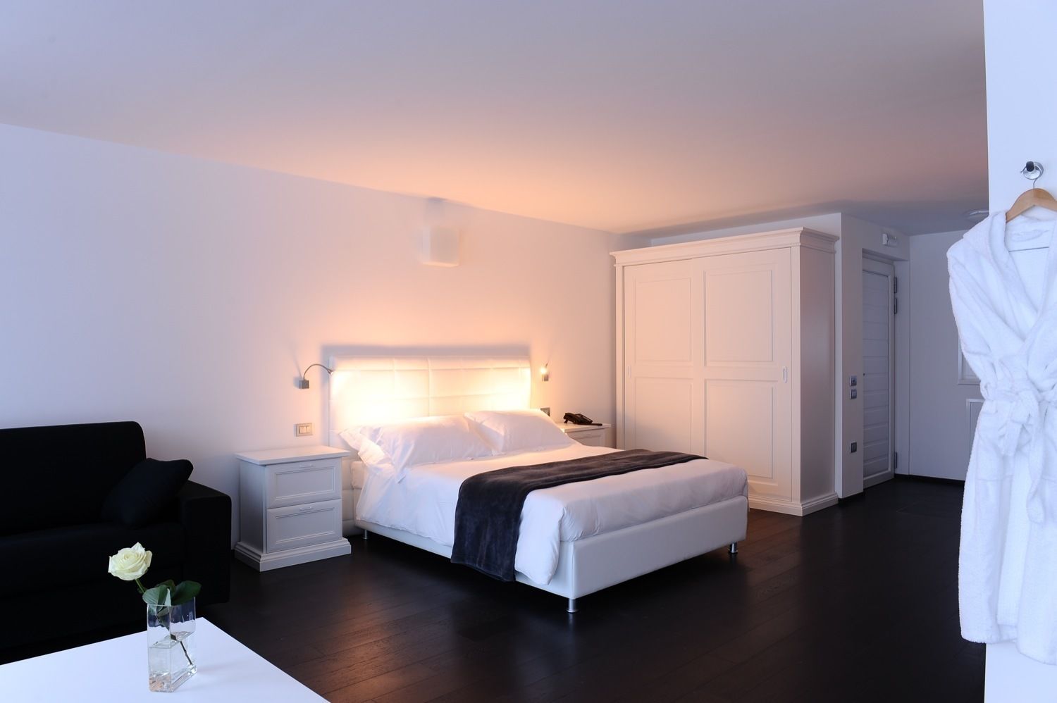 Una habitación de hotel moderna con una cama, mesitas de noche, un armario y una bata colgada en la pared.