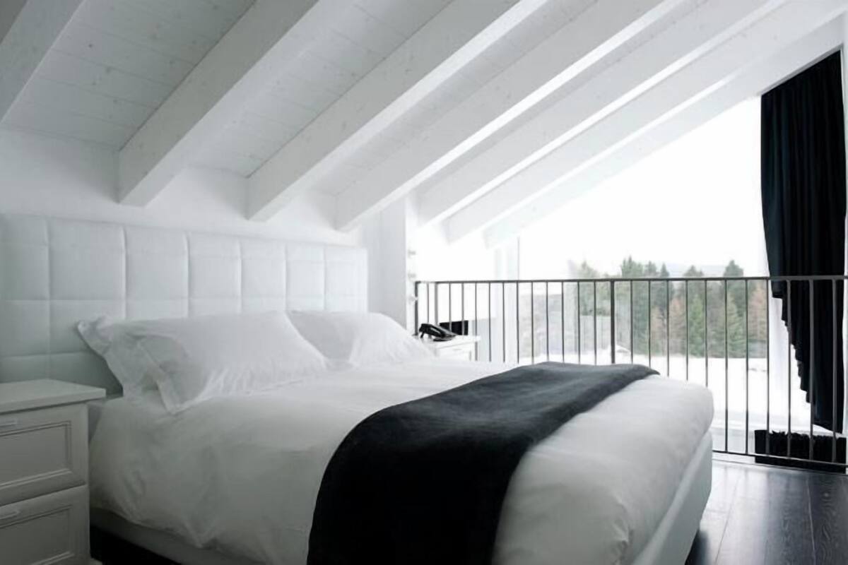 A bedroom with a large bed, a nightstand, and a view of the outdoors through a balcony.