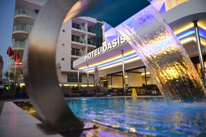 Ein Hotel namens „HOTEL OASIS“ mit Poolbereich und Liegestühlen.