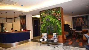 A hotel lobby with a reception desk, a seating area with chairs, a green vertical garden, and a dining area with tables and chairs. - Oasis Otel (Marmaris)