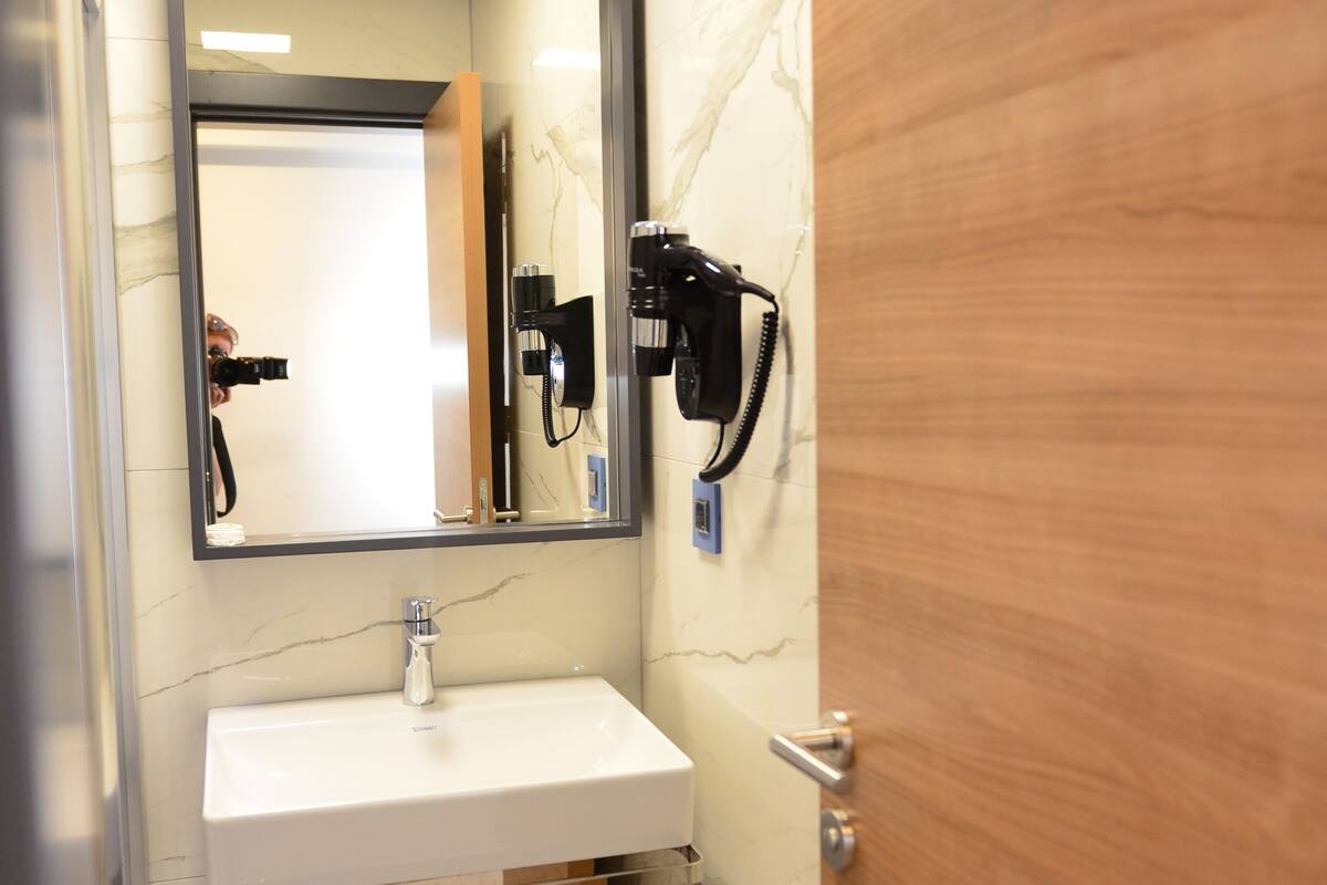 A bathroom with a white sink, a mirror, a hairdryer, and a door.