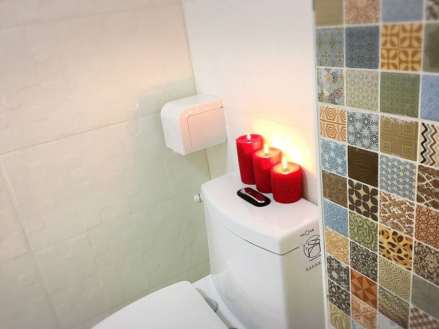 A toilet with three red candles on the tank and a patterned tile wall.