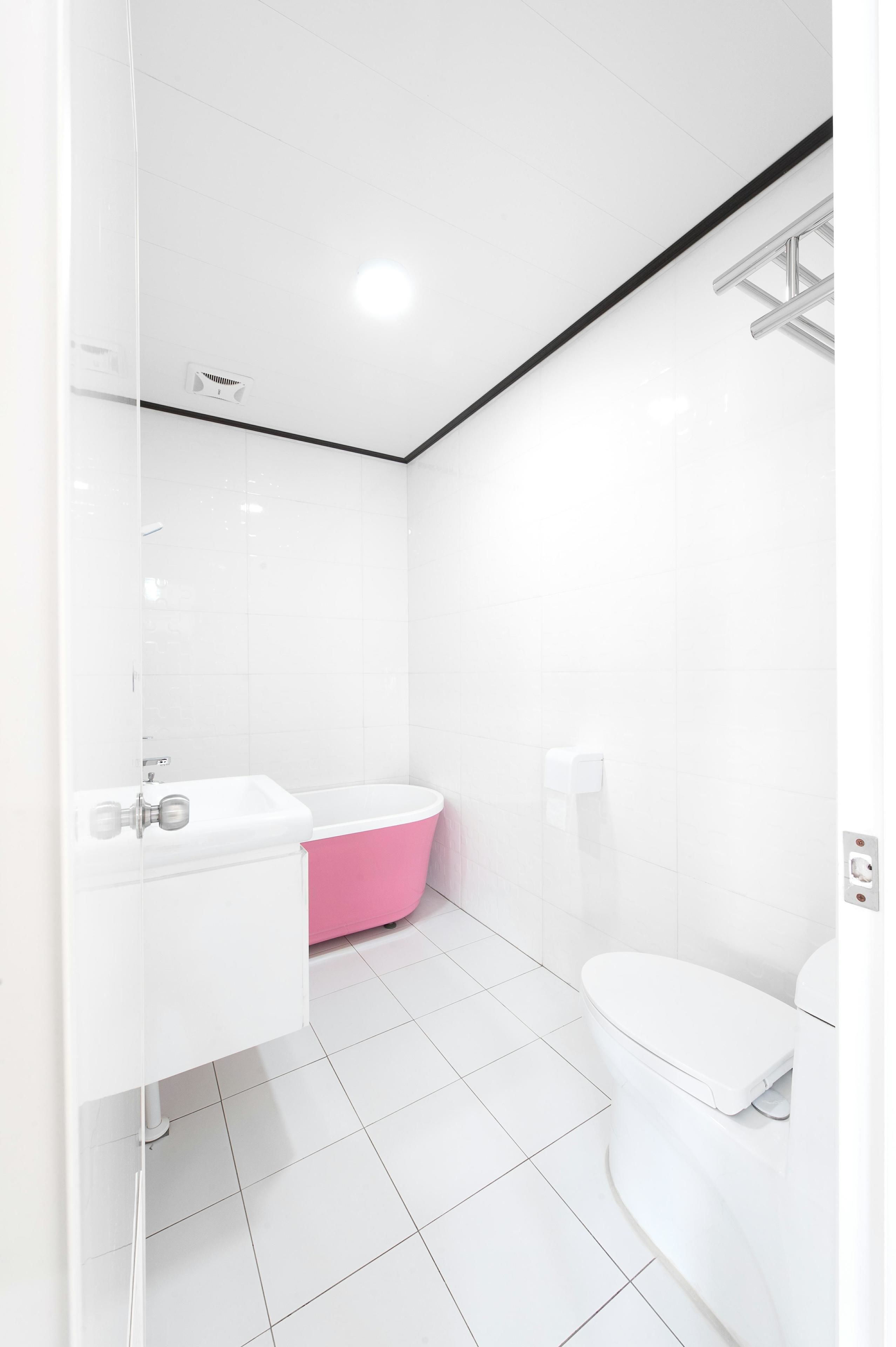 Un baño moderno con un lavamanos blanco, una bañera rosa y un inodoro blanco.