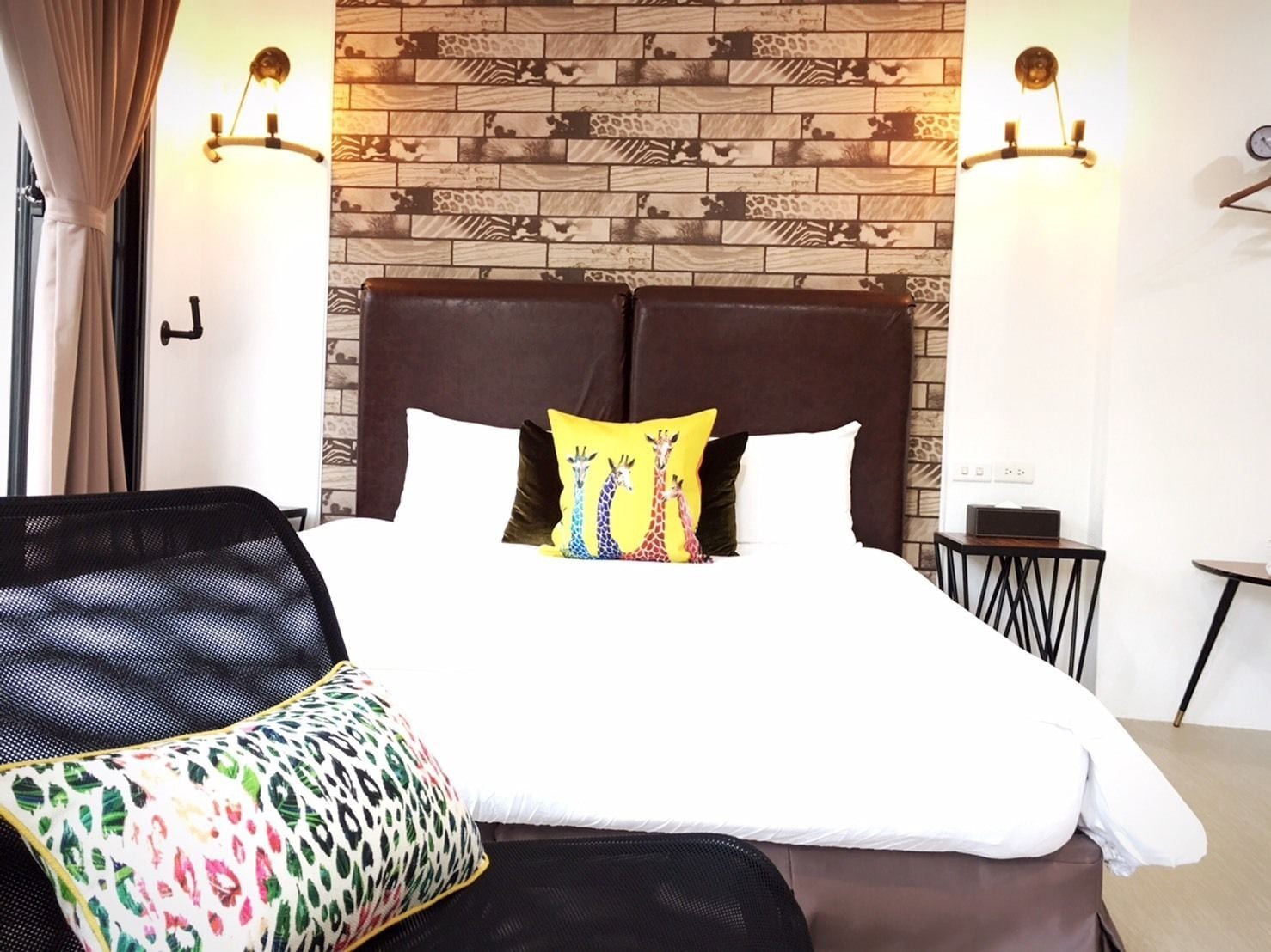 Een hotelkamer met een groot bed, twee wandlampen, een tafeltje en een stoel.