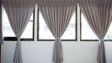 A room with three windows, each with a grey curtain tied back to reveal the outside.