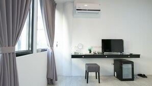 A modern hotel room with a large window, an air conditioning unit, a flat-screen TV, a small refrigerator, a desk with a computer, and a chair. - Live in the happiness (Zhushan)