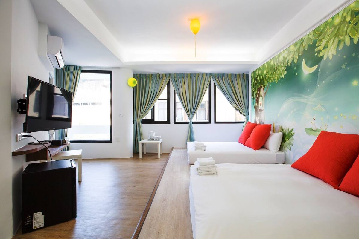 A hotel room with a bed, a TV, a desk, and a window with curtains.