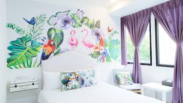 A bedroom with a large bed, a desk, and a chair. There is a window with purple curtains and a wall mural with tropical plants and animals.