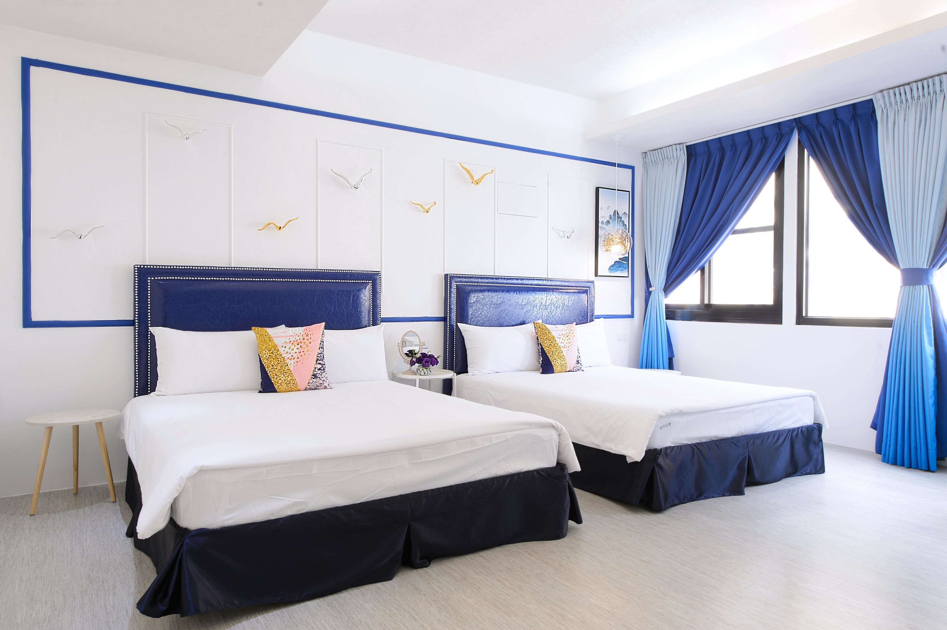 Una habitación de hotel con dos camas, una mesita y un ventanal con cortinas azules.