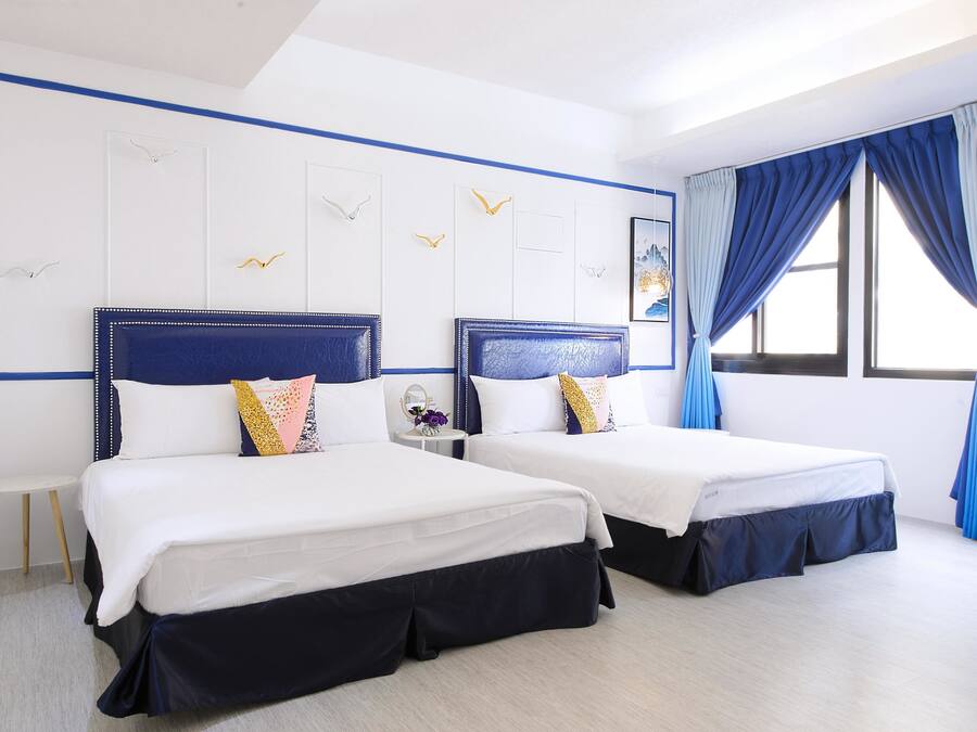 Una habitación de hotel con dos camas, una mesita y un ventanal con cortinas azules.