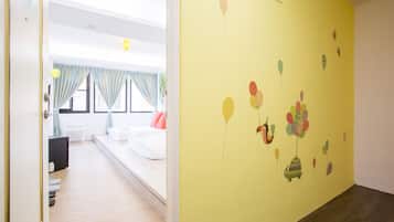 A hotel room with a bed, a desk, and a window with curtains. The room has a yellow wall with a balloon mural.