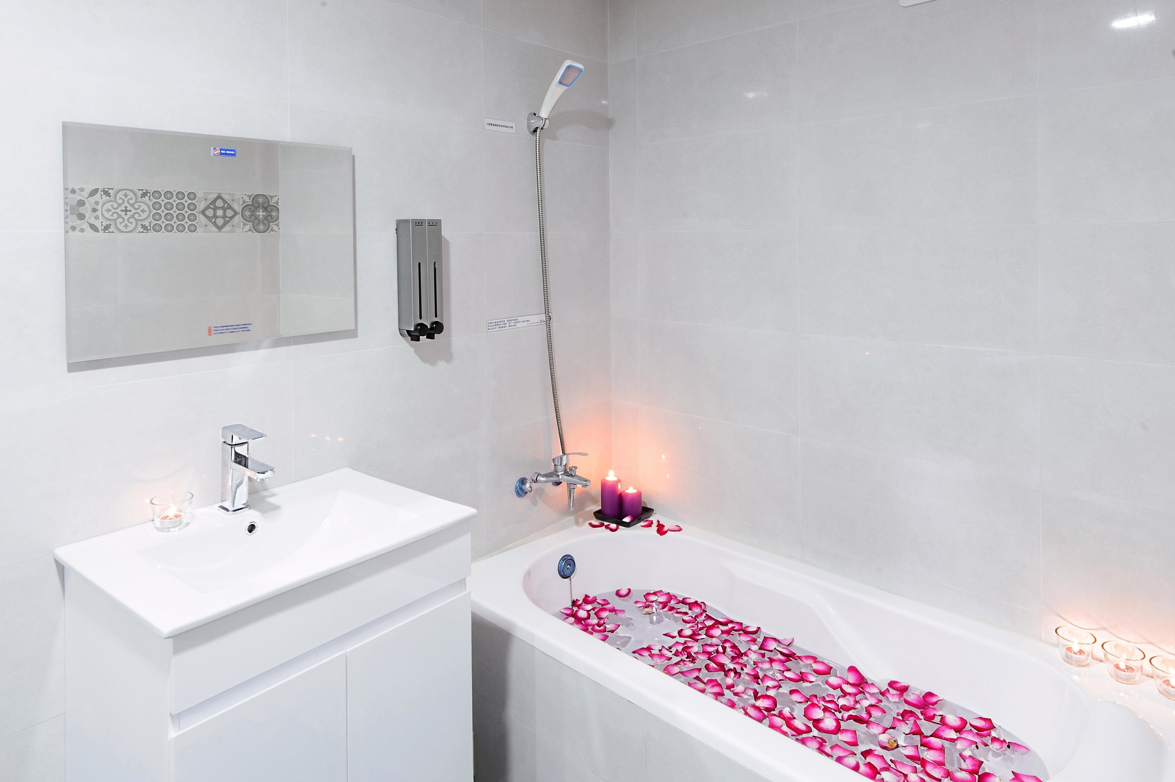 Une salle de bain moderne avec un lavabo blanc, une baignoire remplie de pétales de roses et une douche.