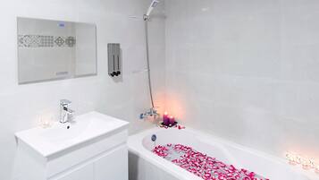 Une salle de bain moderne avec un lavabo blanc, une baignoire remplie de pétales de roses et une douche.