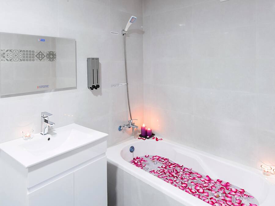 A modern bathroom with a white sink, a bathtub with rose petals, and a shower.