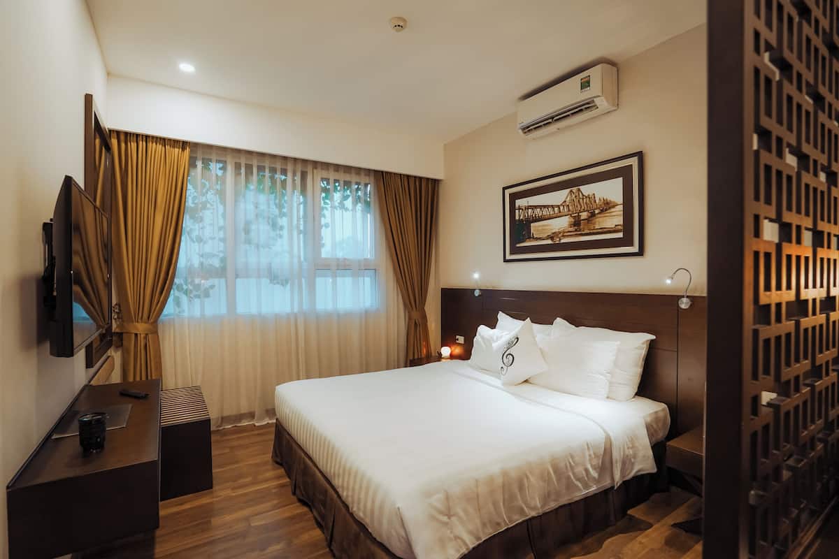 A hotel room with a large bed, a TV, a desk, and a window with curtains.