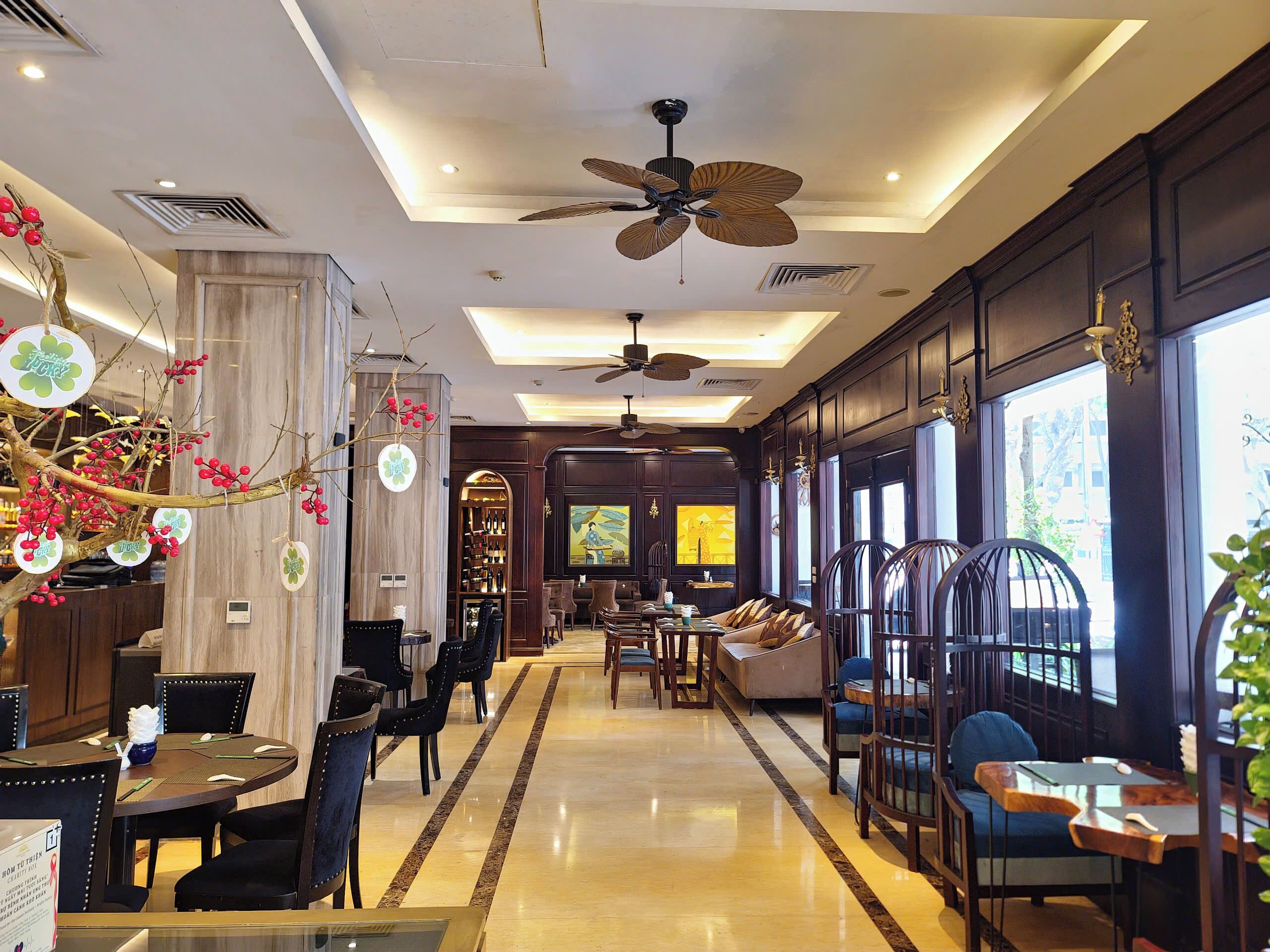 A hotel lobby with a high ceiling, a central ceiling fan, a bar area, and a seating area with tables and chairs.