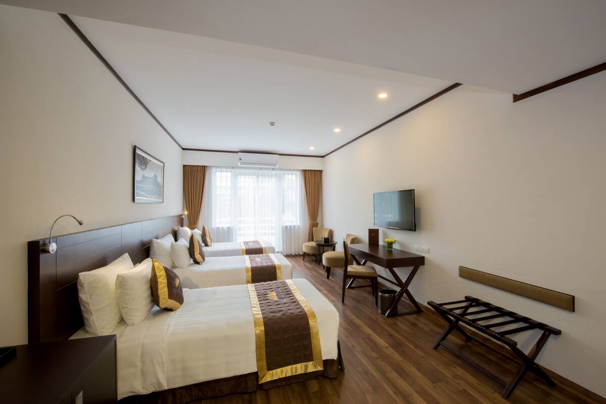 A hotel room with two beds, a desk, a chair, a TV, and a window with curtains.
