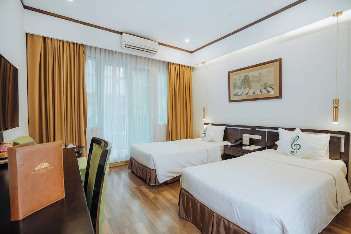 A hotel room with two beds, a desk, a chair, and a painting on the wall.