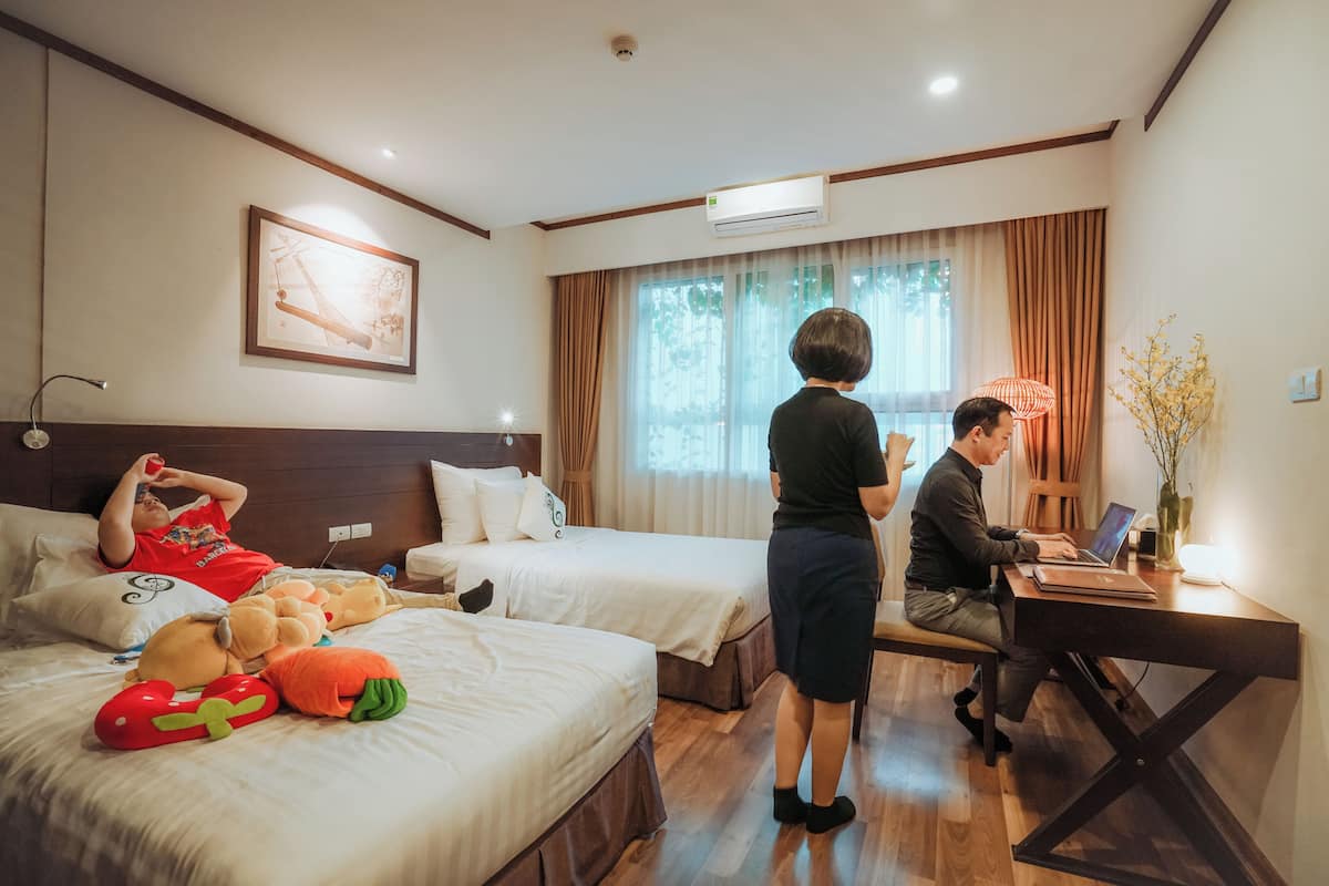 A hotel room with two beds, a desk, and a window with curtains.