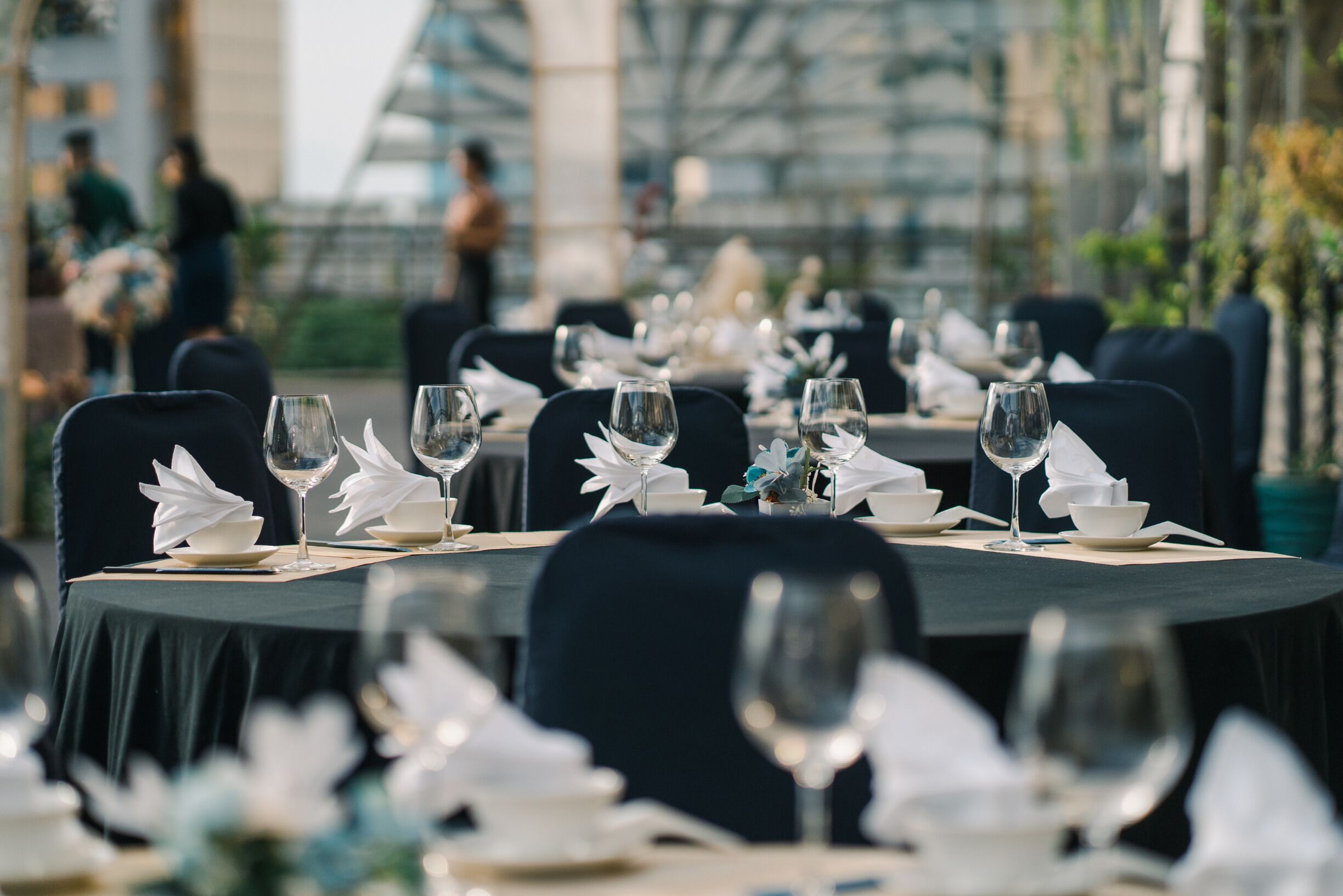 A dining area with round tables set for a meal, featuring white napkins and clear glassware.