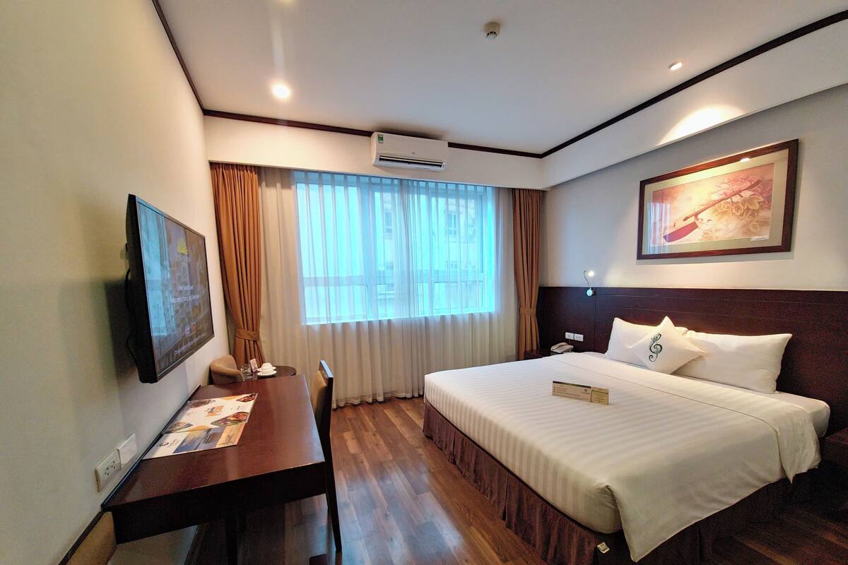 A hotel room with a bed, a desk, a chair, a television, and a window with curtains.