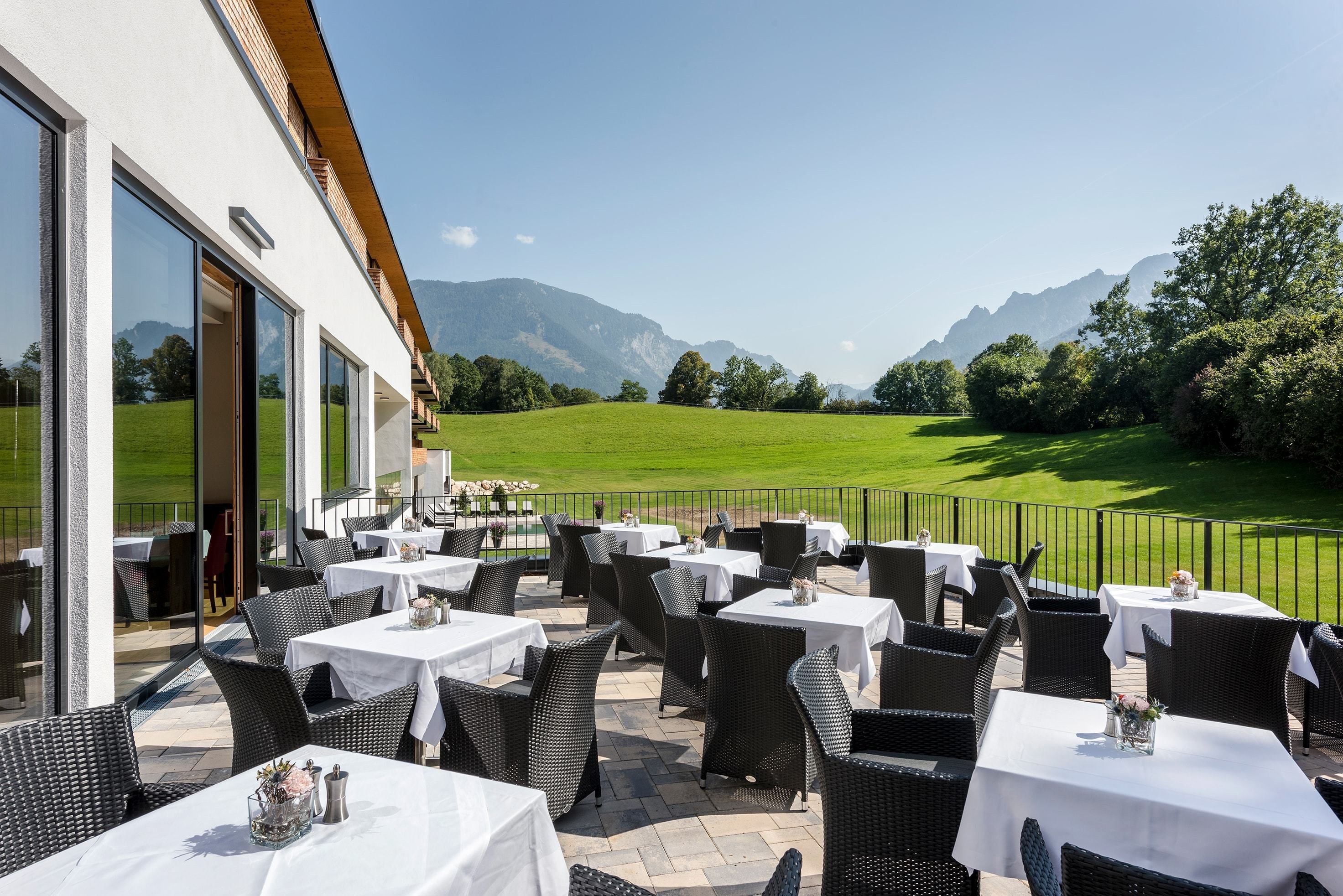 Un patio al aire libre con mesas y sillas, con vistas a un campo verde y montañas.