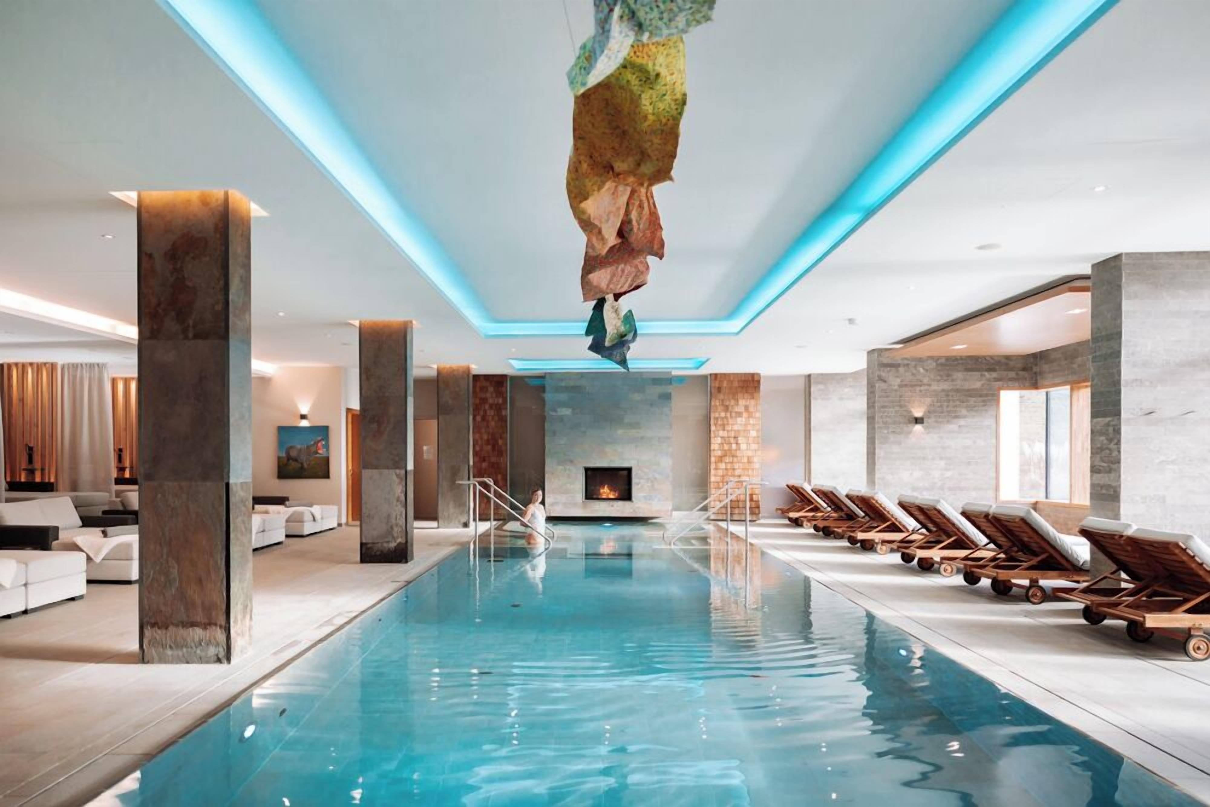 Ein moderner, überdachter Swimmingpool mit klarem, blauem Wasser, Liegestühlen entlang der Seiten und einem Wasserfall im Zentrum.
