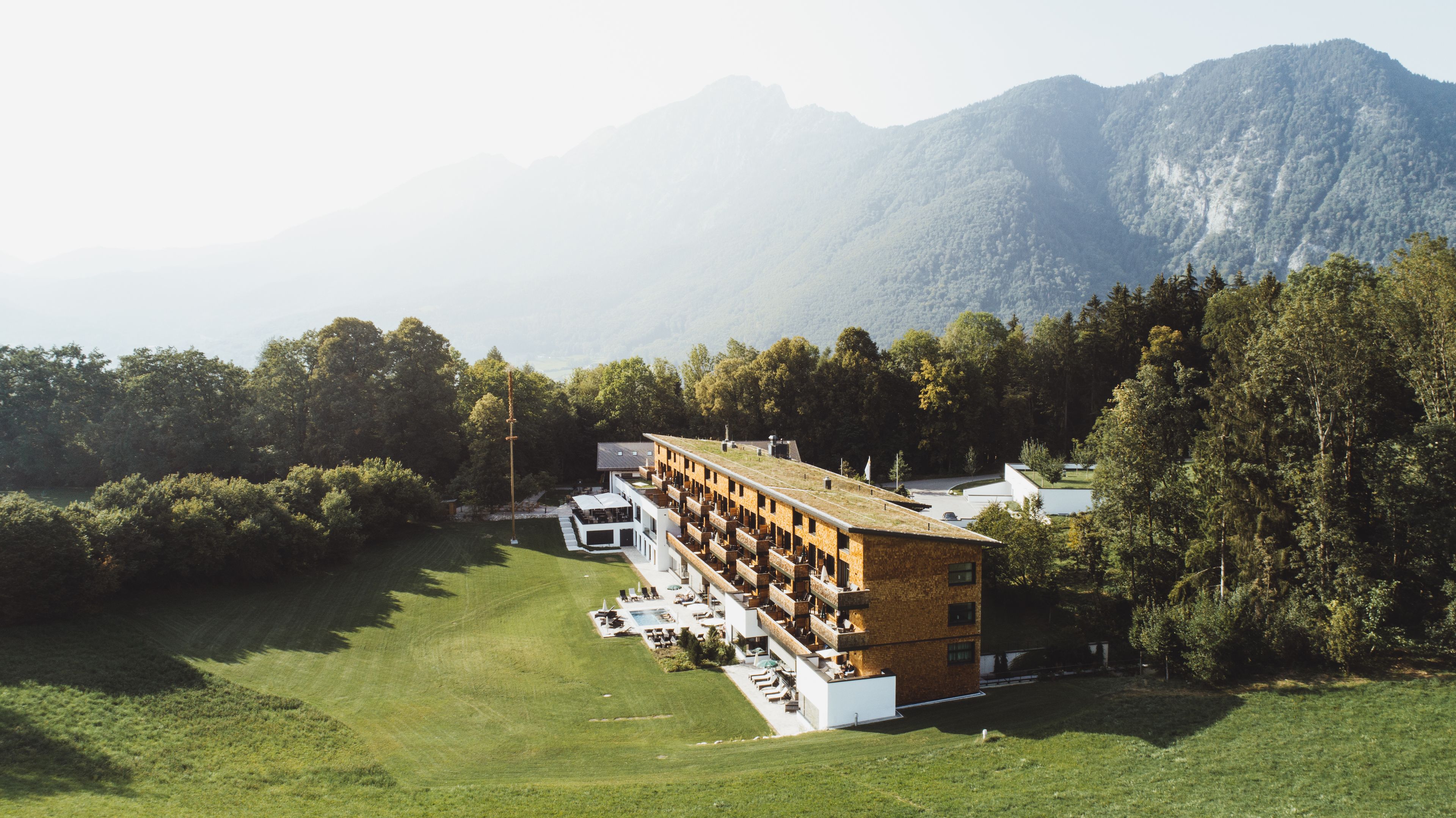 A hotel with a long, multi-story building, a swimming pool, and a lush green lawn.