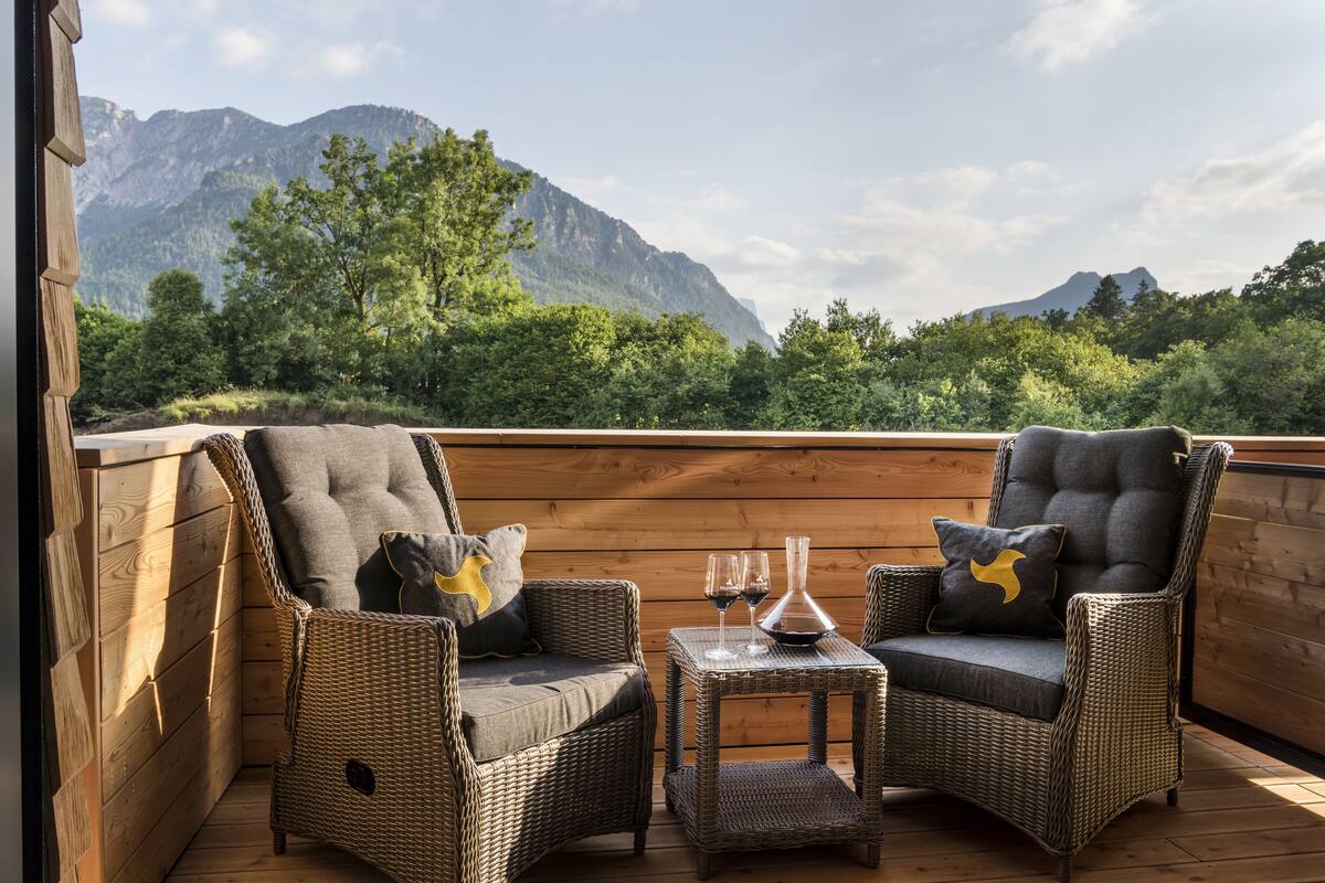 A wooden deck with wicker chairs and a table, overlooking a mountainous landscape.