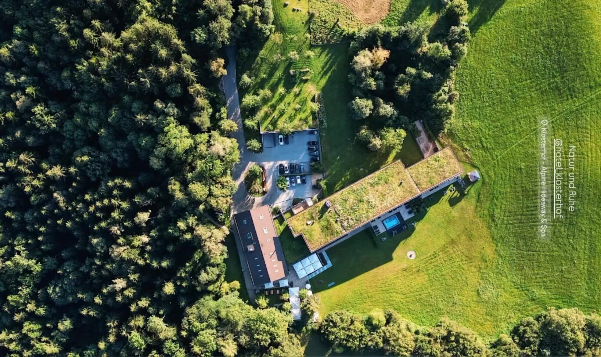 Vista aérea de una propiedad con edificio principal, piscina y campos verdes circundantes.