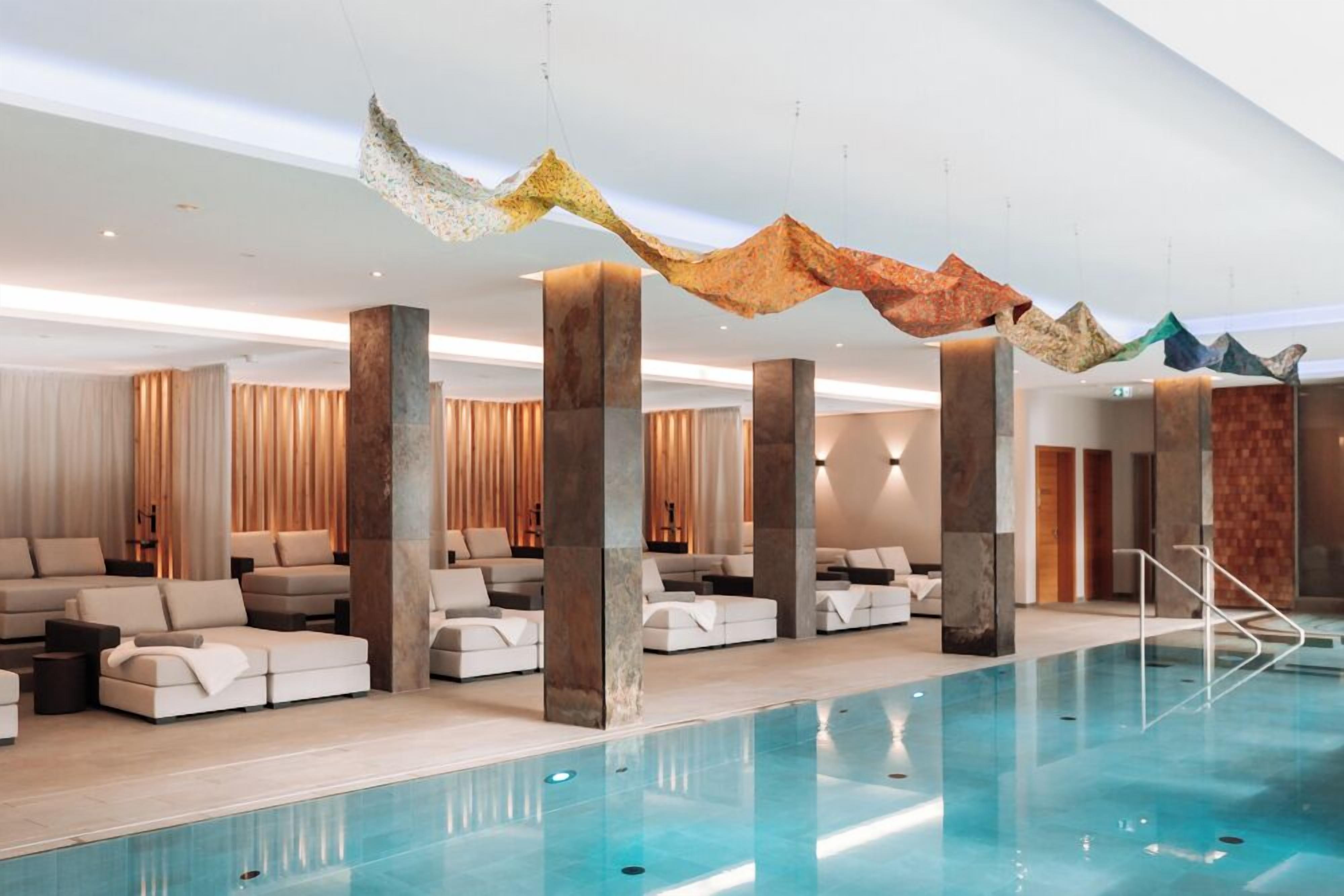 A modern indoor pool area with lounge seating and decorative fabric elements.