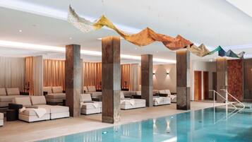 A modern indoor pool area with lounge seating and decorative fabric elements.