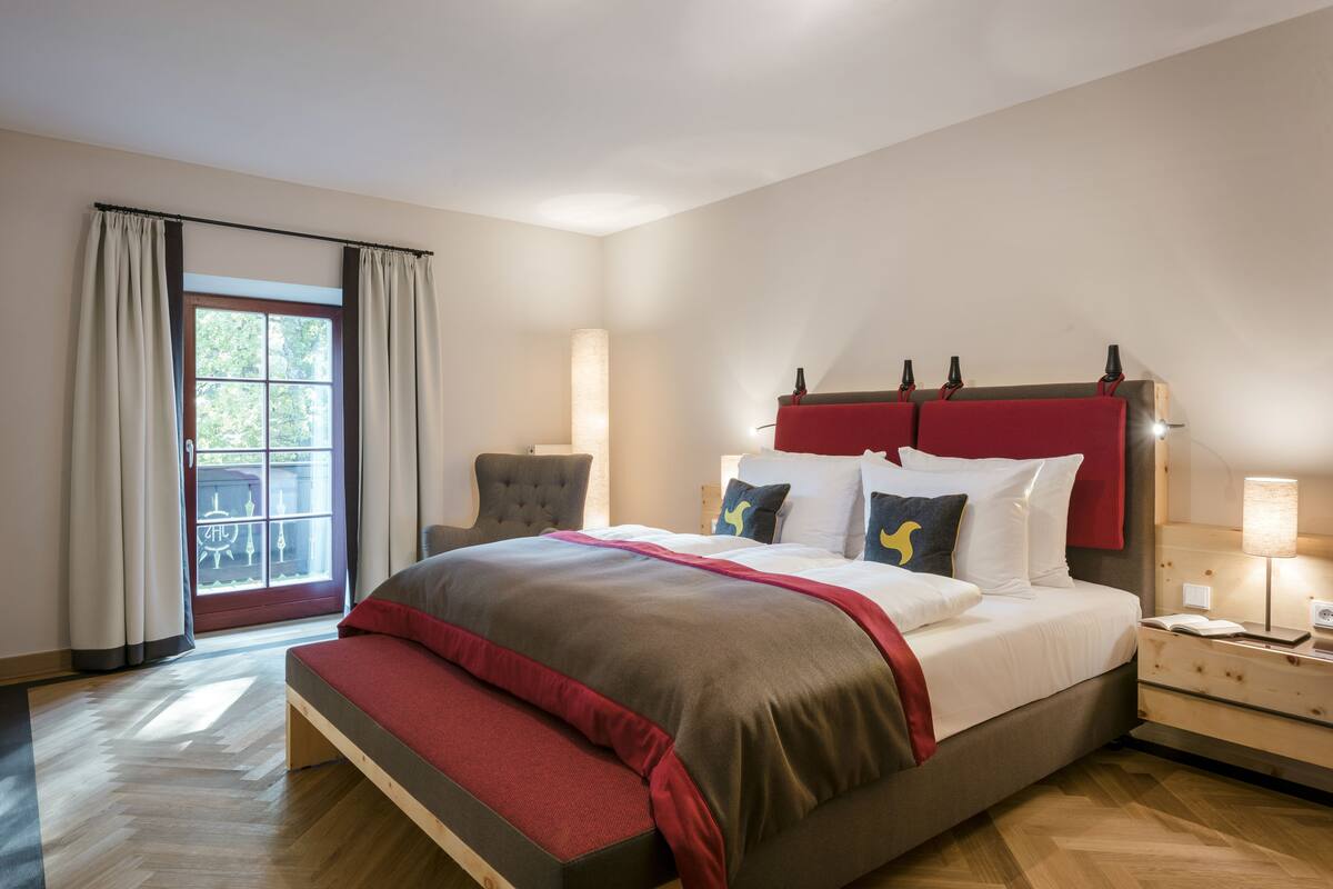 A bedroom with a bed, nightstand, lamp, and window with curtains.