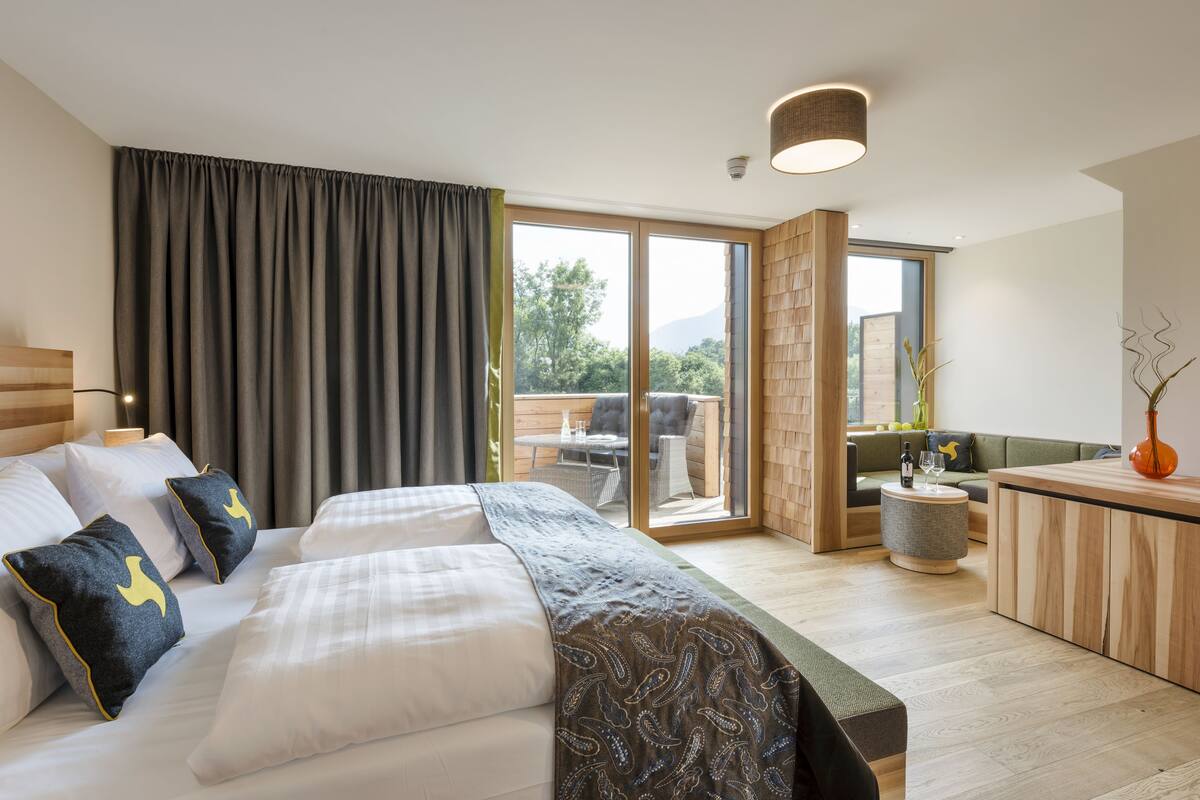A modern hotel room with a large bed, a small round table, and a balcony with a view of the outdoors.