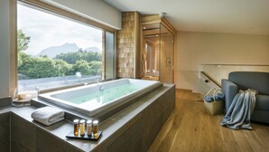 A modern bathroom with a large bathtub, a glass shower enclosure, and a view of a mountainous landscape. - Klosterhof - Alpine Hideaway & Spa (Bayerisch Gmain)